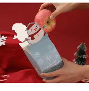 Putting apple into a blue snowman Christmas gift box on festive red background