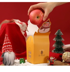 Detail of hand placing a red apple into the yellow gingerbread man Christmas gift box
