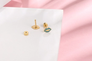 Close-up of lip-shaped enamel earrings with secure gold screw backs on pink silk fabric