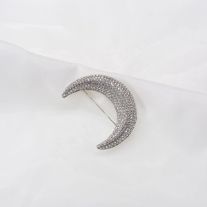 Macro shot of silver crescent moon brooch with pavé rhinestones on white silk fabric