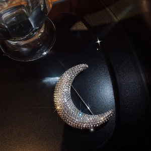 Detailed close-up of a crescent moon brooch encrusted with shimmering crystals on black