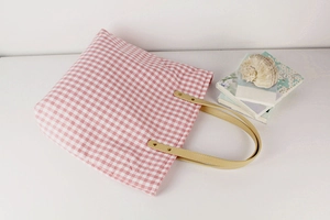 Detail of pink gingham canvas tote bag with faux leather straps and rivet accents