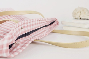 Detailed view of pink plaid canvas tote with leather straps and metal zipper closure