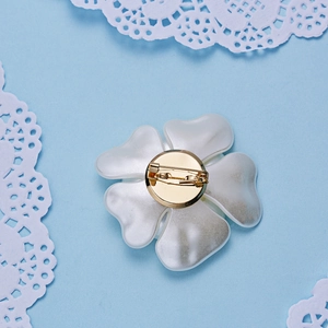 Vue arrière d'une broche fleur avec base en métal doré et épingle sur fond de dentelle