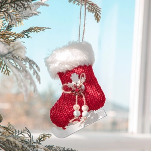 Red knitted Christmas ice skate stocking with white faux fur trim on a snowy pine branch