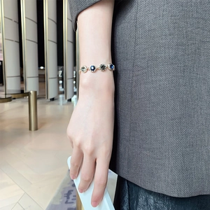 Close-up of gold-plated bracelet featuring blue and taupe gems worn on female wrist
