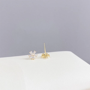 Detail shot of golden flower stud earrings with sparkling cubic zirconia on a white surface