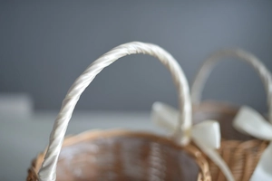 Close-up of woven flower basket handle wrapped in white silk ribbon and natural textures