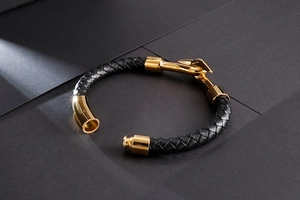 Detail of black braided leather men's bracelet with gold hook and magnetic metal clasp