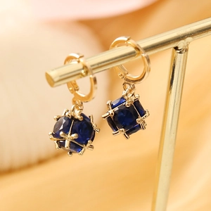 Macro detail of geometric gold earrings featuring deep blue square crystal pendant drops