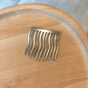 Detail eines silbernen Haarkamms mit 10 gewellten Zähnen auf einem Holztablett