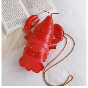 Top view of creative red lobster-shaped crossbody bag with gold chain on white fabric