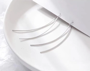 Close-up of curved silver S925 tassel earrings on white display card and ceramic plate