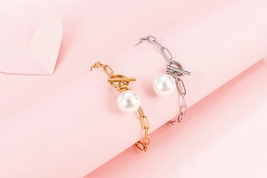 Detail of gold and silver paperclip link bracelets with single pearl charms on pink background
