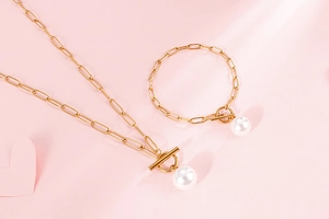 Detailed view of gold paperclip chain necklace and bracelet set with white pearl on pink