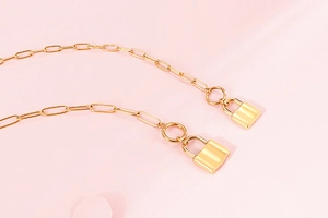 Close-up of golden titanium steel chain with delicate padlock pendants on pink background
