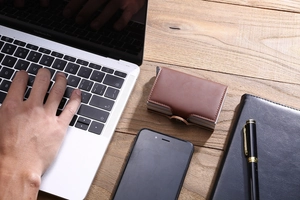 Brown PU leather dual card wallet on a wooden desk with a laptop in a business setting