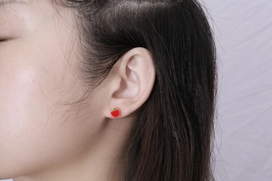 Close-up of red apple stud earrings with green leaf detail worn on the earlobe