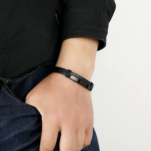 Close-up of a men's black braided leather bracelet with a polished metal plate on wrist