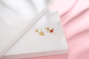 Detail view of gold butterfly stud earrings with red enamel finish and butterfly backs