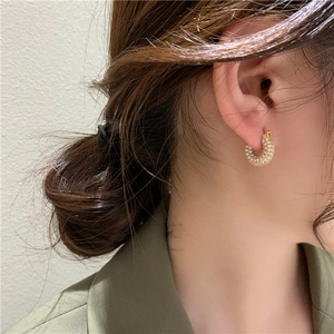 Close-up of golden C-shaped hoop earrings with micro-pave zircons worn by a model