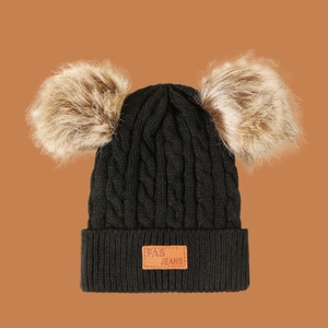 Macro detail of black cable knit hat featuring dual tan faux fur pom-poms and leather tag