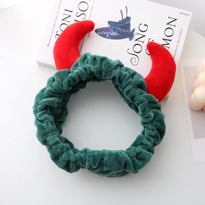 Détail d'un bandeau en peluche verte avec des cornes de diable rouges sur une table