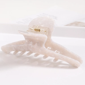 Macro detail of cream acetate hair claw with marble texture on minimalist surface