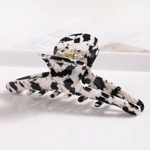 Close-up of a large marbled acetate hair claw clip with a black and white cow print texture