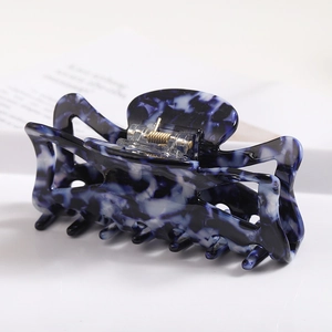 Detail view of large acetate hair claw with deep blue and white marble texture and gold spring
