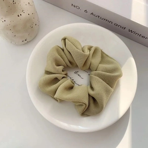 Close-up of a sage green ribbed scrunchie on a white plate with a soft fabric texture