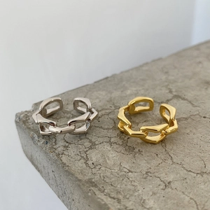 Close-up of gold and silver chunky chain link rings on a textured stone surface