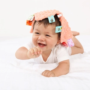 Happy infant with a pink dotted plush security blanket featuring colorful ribbon tags