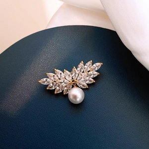 Close-up of golden leaf brooch with sparkling marquise crystals and a white pearl