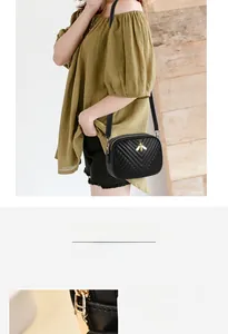 Close-up of golden bee logo on black V-quilted leather crossbody bag with shiny hardware
