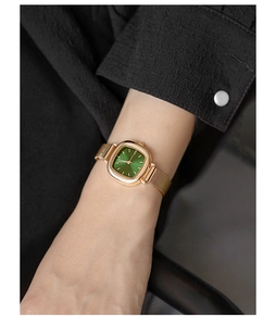 Close-up of a square gold watch with green dial and mesh band worn on a wrist