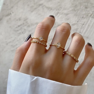 Close-up of four minimalist gold-plated rings with drop-shaped zircon on a model hand