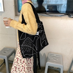 Detail of black canvas tote bag with abstract white line art in a lifestyle street setting