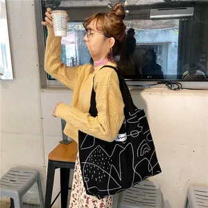 Detail view of large black canvas tote bag with abstract white line art on female model