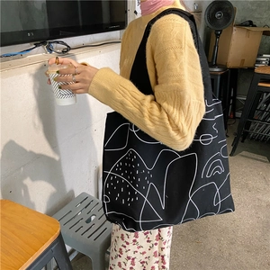 Canvas tote bag with white abstract art pattern shown on shoulder for daily use