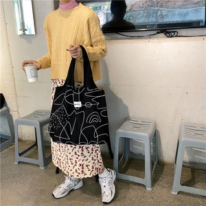 Close-up of black canvas tote bag with white abstract art print carried by model