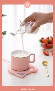 Pink cat-shaped electric cup warmer with mug showing milk pouring in a cozy setting