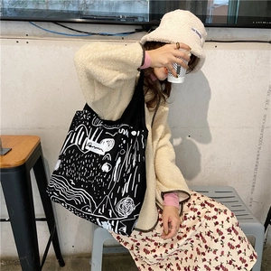 Artistic white graffiti print on a large black canvas tote bag in a street style look