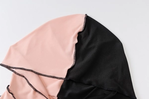 Detail of pink and black knit fabric with contrast overlock stitching on the hooded dress