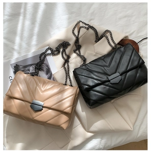 Detail of beige and black quilted crossbody bags with chain straps and metal locks