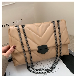 Detail of beige quilted chain bag featuring V-shaped stitching and black metal strap