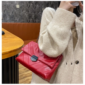 Close-up of red quilted crossbody bag with matte black metal lock and chain strap detail