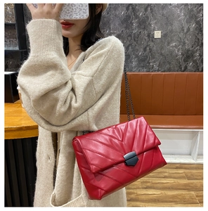 Close-up of red quilted crossbody bag with black metal chain strap and V-pattern stitching