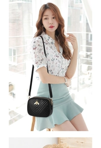 Detail of a black quilted crossbody bag with a golden bee clasp and thin leather strap