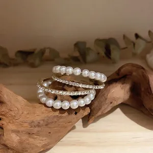 Set of four rings featuring white pearls and pavé rhinestones on gold bands over wood